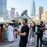 A man with a camera and crew filming a crowd during an Eid event for a video production company.