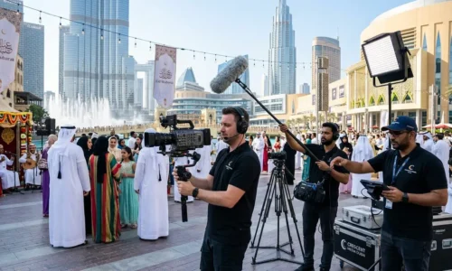 A man with a camera and crew filming a crowd during an Eid event for a video production company.